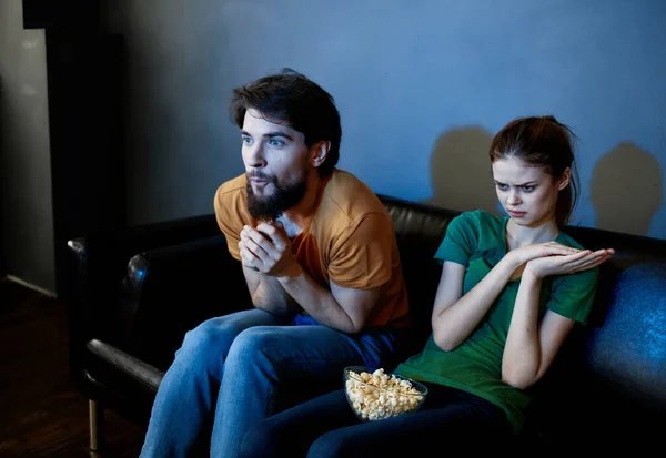 Eine Frau und ein Mann mit Popcorn auf einem Ledersofa drinnen vor dem Fernseher am Abend — Stockfoto