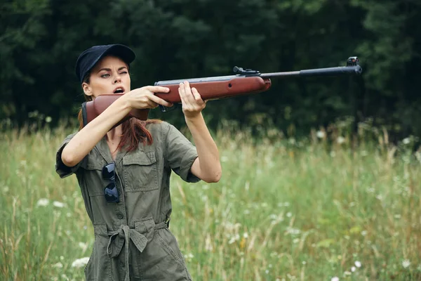 Mulher ao ar livre uma mulher segura uma arma na frente dela apontando para uma caça folhas verdes verde — Fotografia de Stock