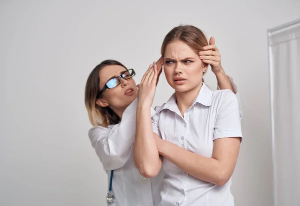 Médico profesional mujer en gafas toca la cabeza del paciente sobre un fondo claro — Foto de Stock