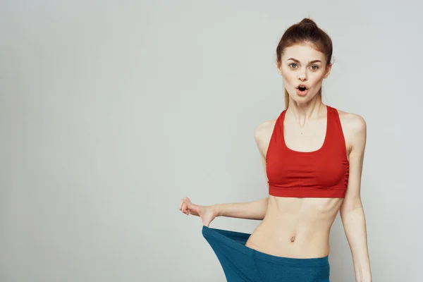 Una mujer con una camiseta roja sobre un fondo claro se dedica a gestos de fitness con las manos una figura delgada —  Fotos de Stock