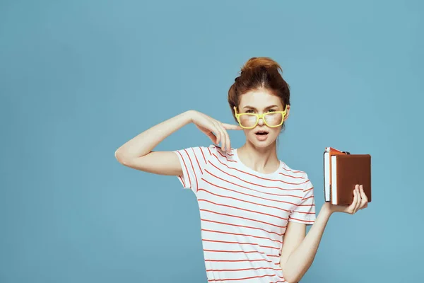 Étudiante avec des livres dans les mains sur un fond bleu et modèle de lunettes jaunes coiffure vue recadrée — Photo