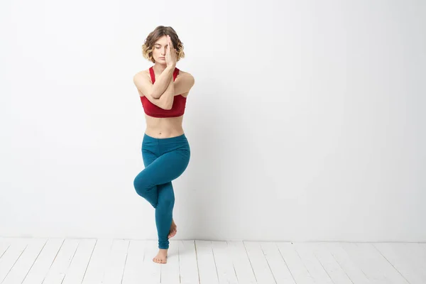 Sport kobieta w jasnym pokoju robi jogę w pełnym wzroście niebieskie legginsy i czerwony tank top — Zdjęcie stockowe