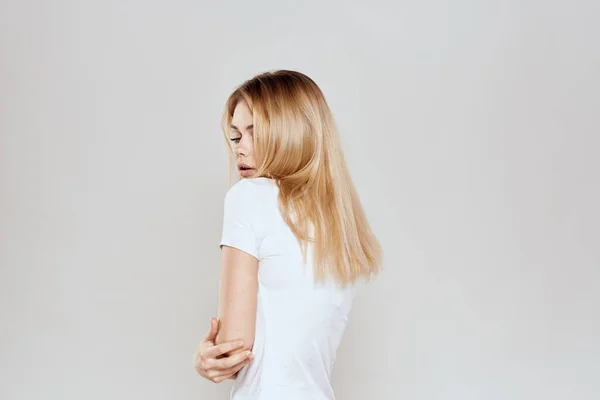 Loira alegre em uma camiseta branca gesticulando com as mãos luz de fundo — Fotografia de Stock