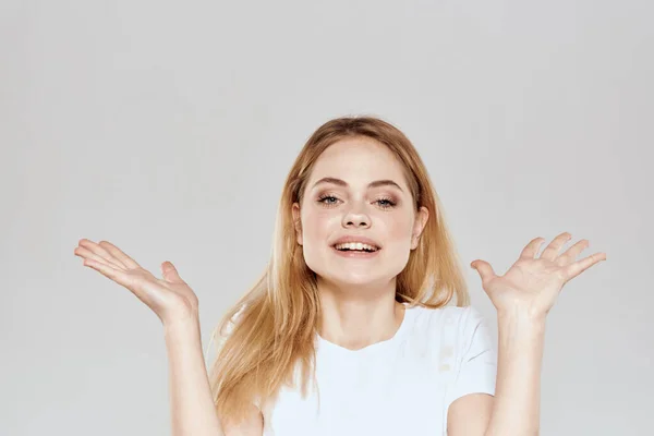 Loira alegre em uma camiseta branca gesticulando com as mãos luz de fundo — Fotografia de Stock