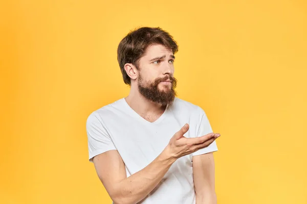 Бородатий чоловік емоції жести руками вираз обличчя біла футболка жовтий фон — стокове фото