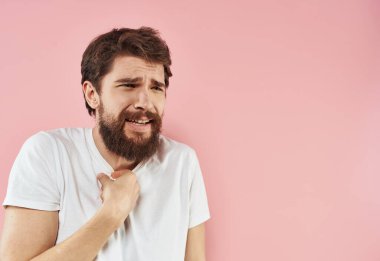 Elleri pembe arka planda, sakallı bir adam beyaz tişörtlü bir adam.