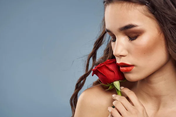 Portrait de femme avec rose rouge près du visage sur fond gris et maquillage cheveux bouclés — Photo