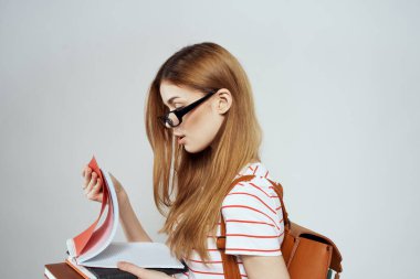 Sırtında not defteri ve sırt çantası olan bayan öğrenci bilim gözlüklerini kırpmış.