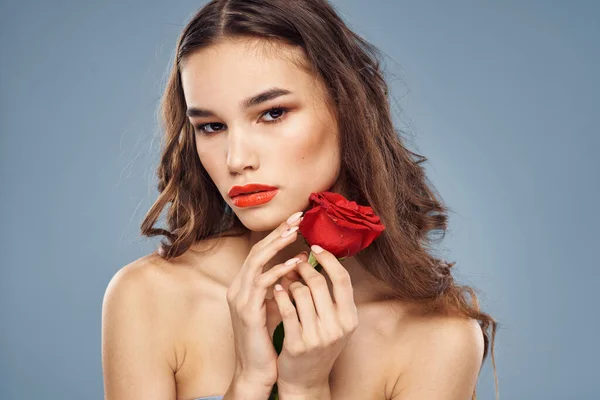 Frauenporträt mit roter Rose in Gesichtsnähe auf grauem Hintergrund und geschminkten lockigen Haaren — Stockfoto