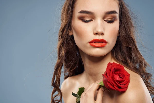 Žena portrét s červenou růží v blízkosti obličeje na šedém pozadí a make-up kudrnaté vlasy — Stock fotografie