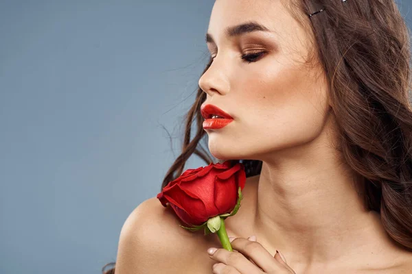 Portrait de femme avec rose rouge près du visage sur fond gris et maquillage cheveux bouclés — Photo