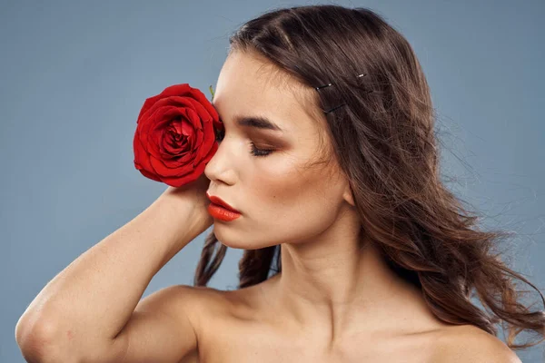 Portrait de femme avec rose rouge près du visage sur fond gris et maquillage cheveux bouclés — Photo