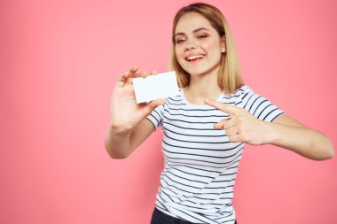 Elinde kartvizit olan bir kadın çizgili bir tişört pembe arka plan fotokopi alanı reklamı