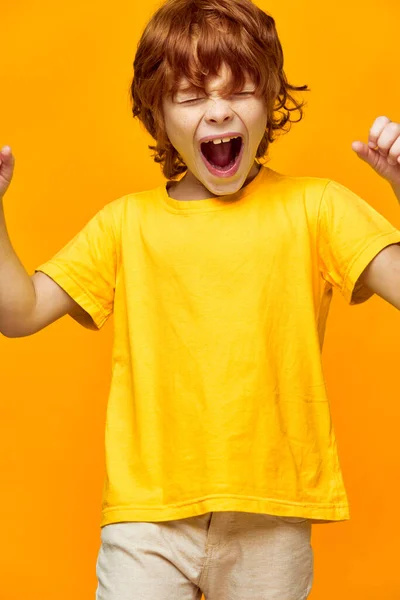 Energetikus gyermek vörös haj sikolyok ellen sárga háttér — Stock Fotó
