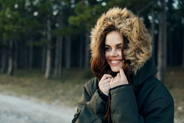 Žena bunda s kapucí úsměv dívat stranou čerstvý vzduch na pozadí lesa — Stock fotografie