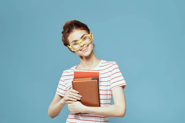 Estudante feminina com livros em mãos em um fundo azul e óculos amarelos modelo penteado corte vista — Fotografia de Stock