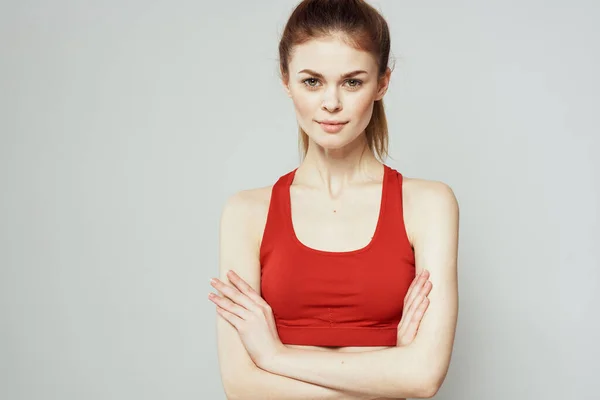 Een vrouw in een rood T-shirt op een lichte achtergrond is bezig met fitness gebaren met haar handen een slank figuur — Stockfoto