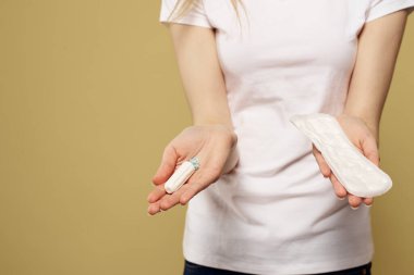 Elinde tampon ve bej arka planda pedi olan beyaz tişörtlü bir kız.