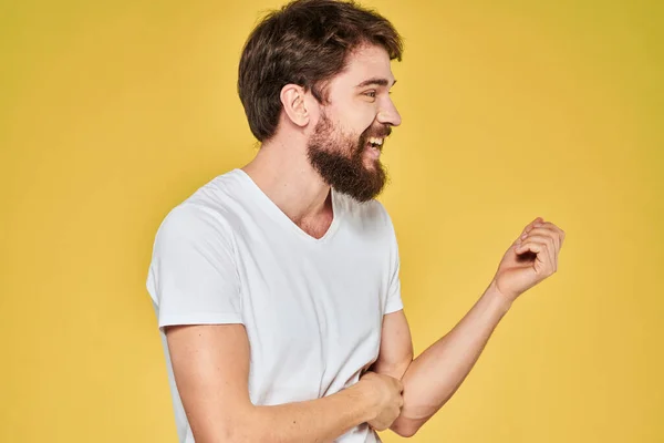 Szakállas férfi fehér póló érzelmek gesztusok kezek szórakoztató sárga háttér — Stock Fotó