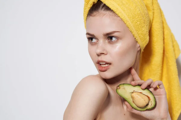 Mulher bonita com abacate nas mãos de uma toalha amarela na cabeça limpa a saúde da pele — Fotografia de Stock