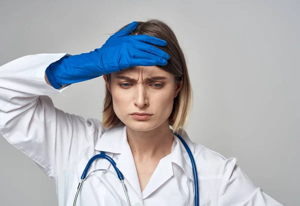 Una enfermera con un vestido médico y guantes azules gestos con un estetoscopio alrededor de su cuello — Foto de Stock