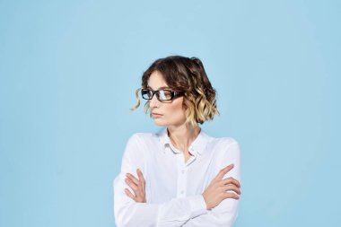 Mavi arka plan gözlüklü, kıvırcık saçlı, açık renk gömlekli iş kadını.