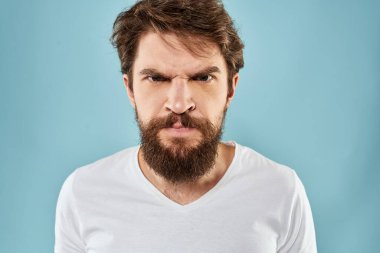 Sakallı adam duyguları, yüz ifadesi el hareketleriyle mavi arka planı kapatır.