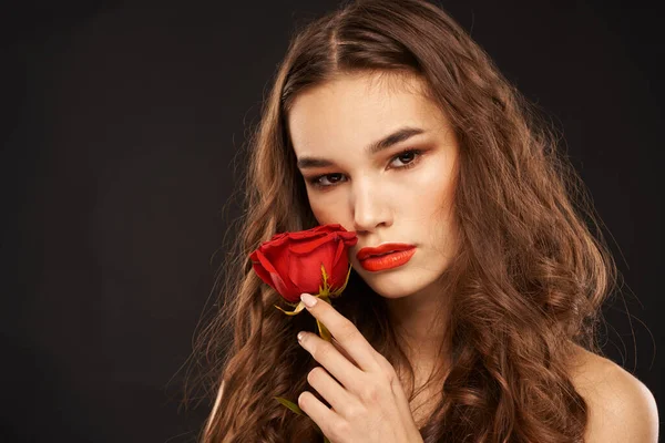 Donna con una rosa rossa su uno sfondo scuro trucco capelli lunghi labbra rosse — Foto Stock