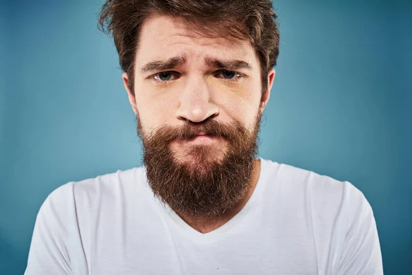 Brodaty mężczyzna niezadowolony osoby ekspresja twarzy emocje zbliżenie niebieski tło biały t-shirt — Zdjęcie stockowe