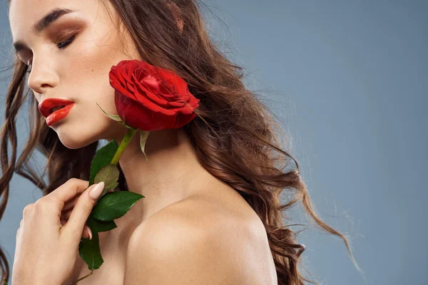 Retrato de una mujer con una rosa roja en sus manos sobre un fondo gris hombros desnudos maquillaje de noche — Foto de Stock