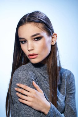 Gri kazaklı, parlak makyajlı, uzun saçlı güzel bir kadın.