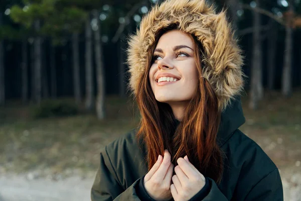 Mujer alegre en una chaqueta con capucha mira hacia arriba sobre el fondo del bosque —  Fotos de Stock