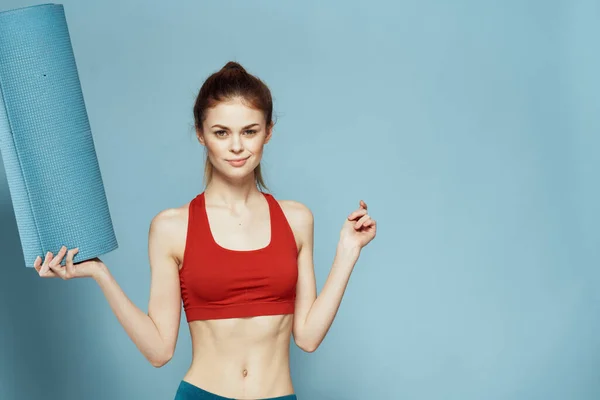Atletische vrouw met fitness mat oefening slank figuur rood t-shirt blauw achtergrond — Stockfoto