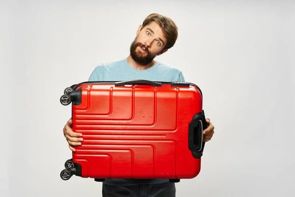 Man on an isolated background holds in his hands a red suitcase on wheels — Stock Photo, Image