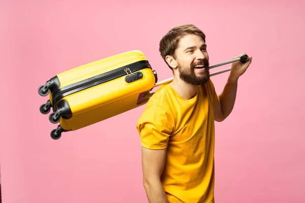 A joyful man on a pink background holds a suitcase on his shoulder — Stock Photo, Image