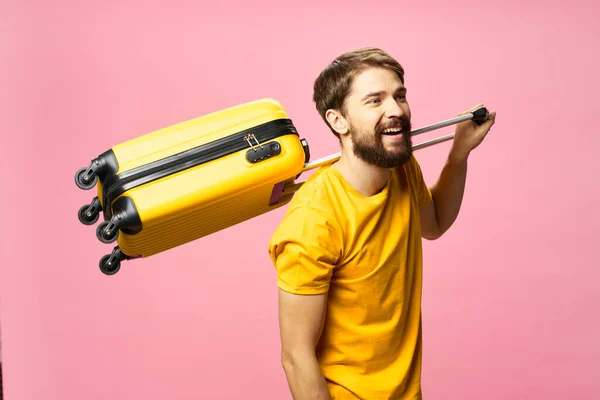 Um homem alegre em um fundo rosa segura uma mala em seu ombro — Fotografia de Stock