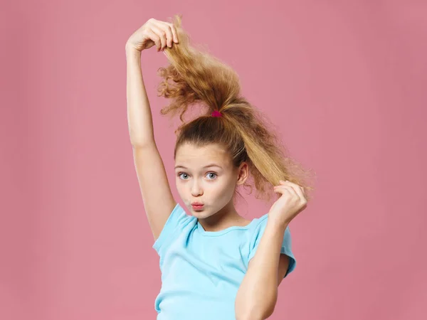Девушка держит косичку за волосы весело голубая футболка розовый фон — стоковое фото