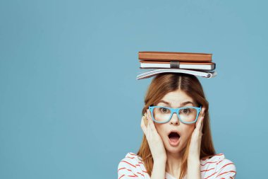 Kafası üzerine kitapları olan kız öğrenci. Bilim eğitimi almış. Mavi arka plan duyguları elleriyle hareket ediyor.