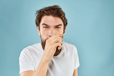 Huysuz yüz ifadesi olan bir adam. Stüdyo tarzı mavi arka planda el kol hareketi yapıyor.