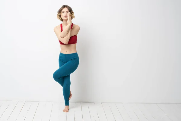 Wanita olahraga di ruang cerah melakukan yoga dalam pertumbuhan penuh legging biru dan atas tangki merah — Stok Foto