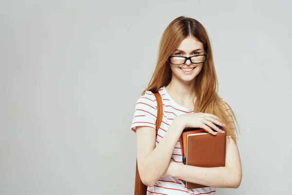 Estudante feminina com bloco de notas e óculos em um fundo leve vista cortada de uma camiseta listrada — Fotografia de Stock