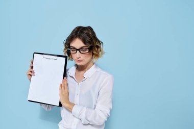 Mavi arka planda bir klasörde evrakları olan ve yüzünde açık renk gözlüklü bir iş kadını.