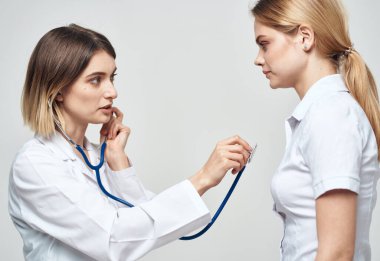Steteskoplu bir doktor beyaz tişörtlü bir kadını muayene ediyor.