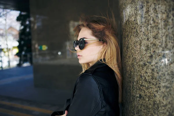 Kobieta stoi pod mostem na ulicy w okularach przeciwsłonecznych i skórzanej kurtce — Zdjęcie stockowe
