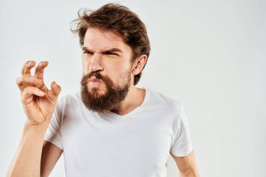 El kol hareketleri yapan sakallı bir adam. Beyaz tişört, stüdyo, duygu, ışık arka plan.