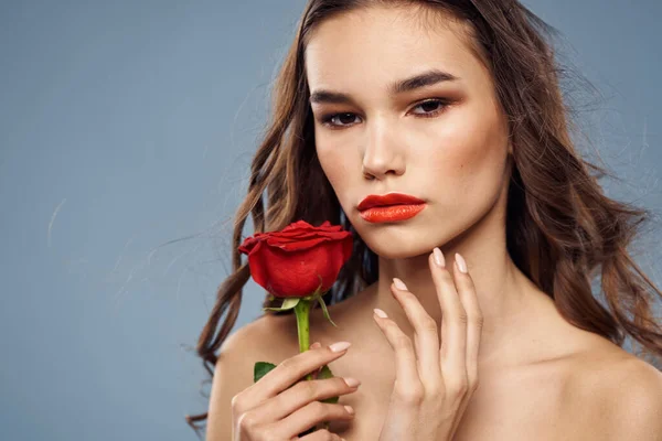 Vrouw portret met rode roos in de buurt van het gezicht op grijze achtergrond en make-up krullend haar — Stockfoto