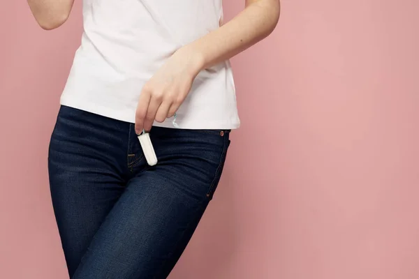 Mulher com um tampão na mão dias críticos higiene branco t-shirt jeans rosa fundo ciclo menstrual — Fotografia de Stock