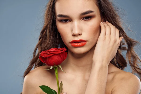 Žena portrét s červenou růží v blízkosti obličeje na šedém pozadí a make-up kudrnaté vlasy — Stock fotografie