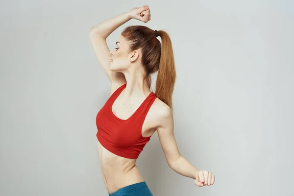 Een vrouw in een rood T-shirt op een lichte achtergrond is bezig met fitness gebaren met haar handen een slank figuur — Stockfoto
