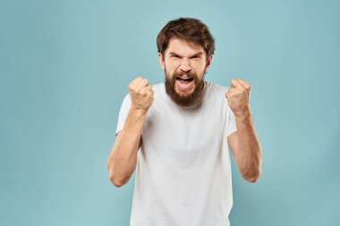 Erkekler elleriyle hareket eder. Duyguları hoşnutsuzdur. Beyaz tişört mavi arka plan.